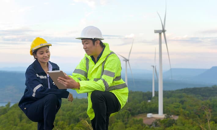 Man and woman referencing a tablet with windmills in the background.