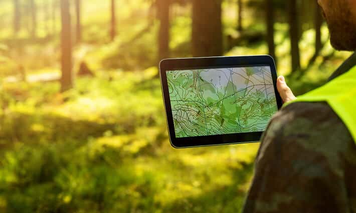 Man holding a tablet with a topological map in nature.
