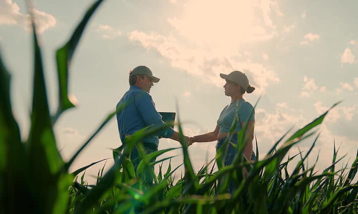 A man and woman shaking hands in a field.
