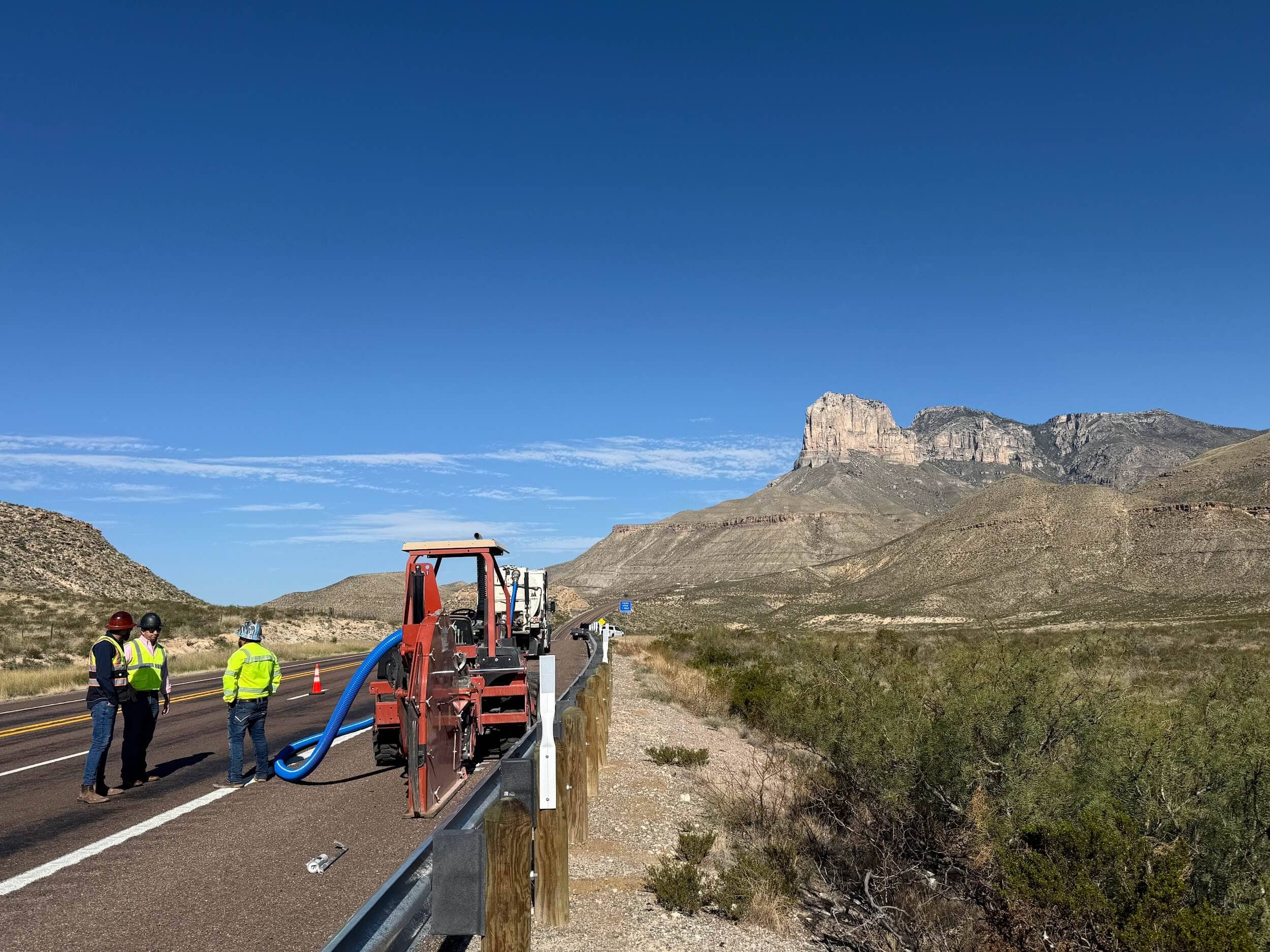 broadband lines being laid on side of road in desert with construction workers