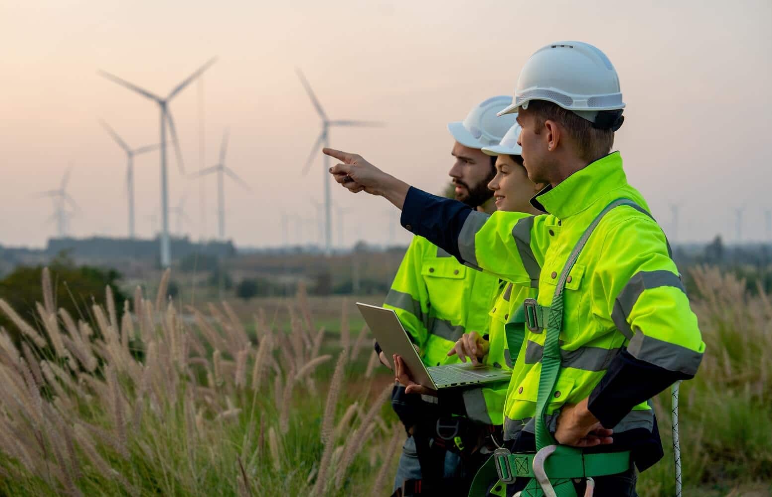 ESE Partners environmental consultants in Texas reviewing site data on a laptop in the field near a wind energy installation, with multiple wind turbines visible in the background