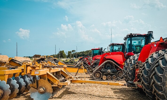 Heavy farm tractors and disc harrow equipment parked on dirt lot