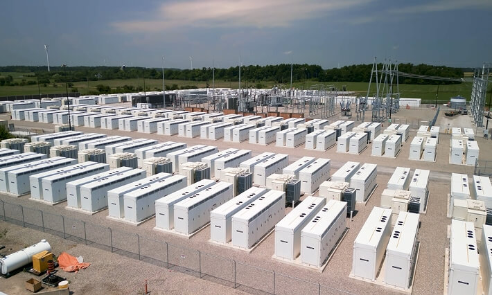 Rows of white battery storage and generator units at fenced power facility